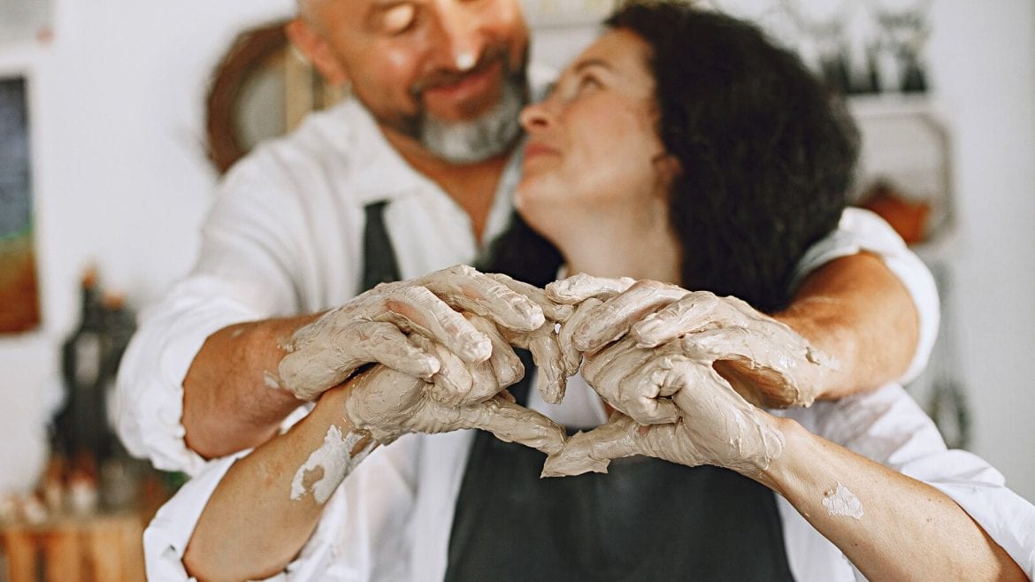 A couple with their hands covered in clay, working on pottery together