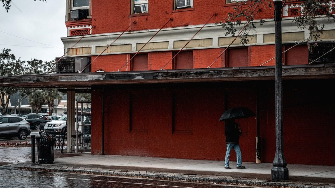 A person holding an umbrella walks on a sidewalk next to a red brick building