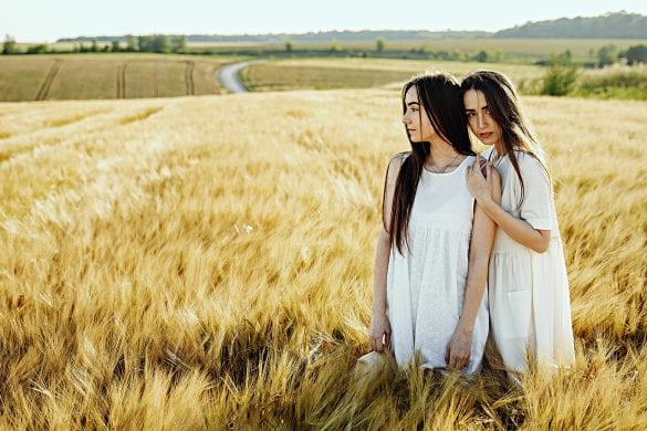 Two women standing in a wheat field, looking in different directions with a serene expression