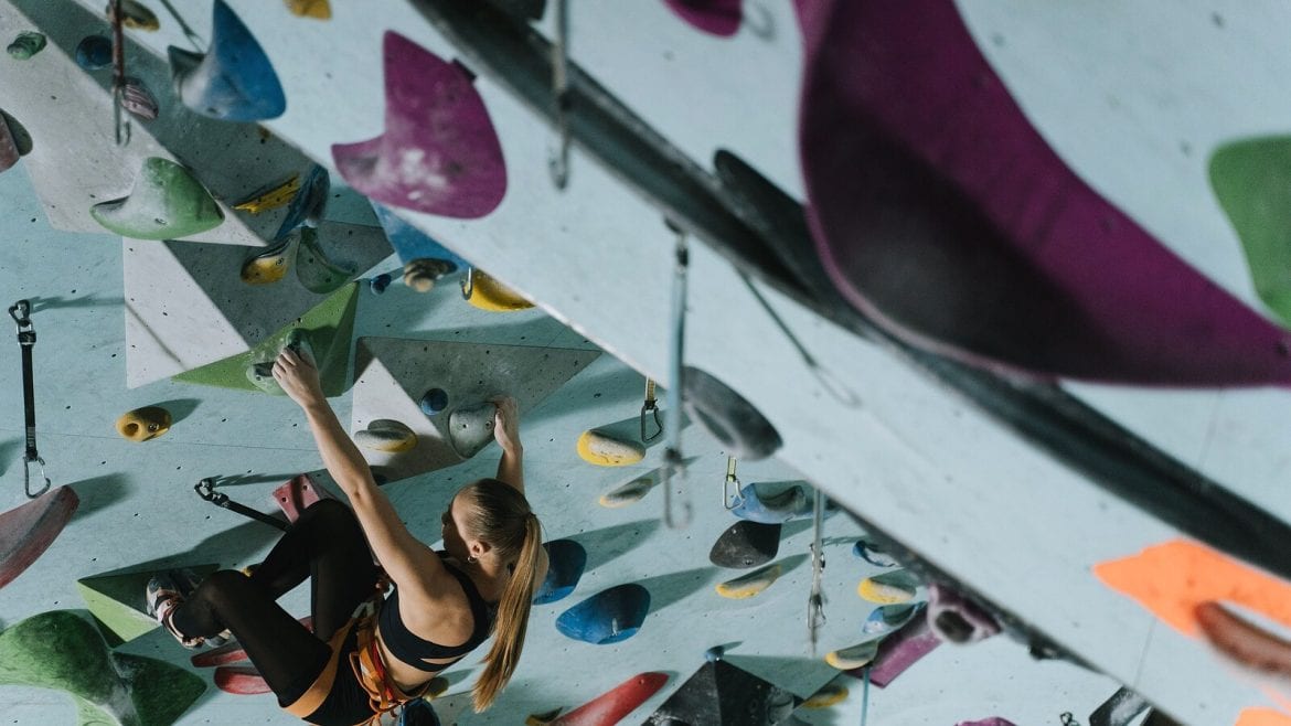 A woman is climbing an indoor climbing wall, using colorful holds. She appears to be focused on her progress
