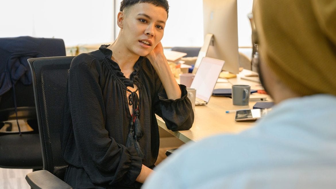 A person sitting at a desk in an office environment, facing another person who is not visible in detail