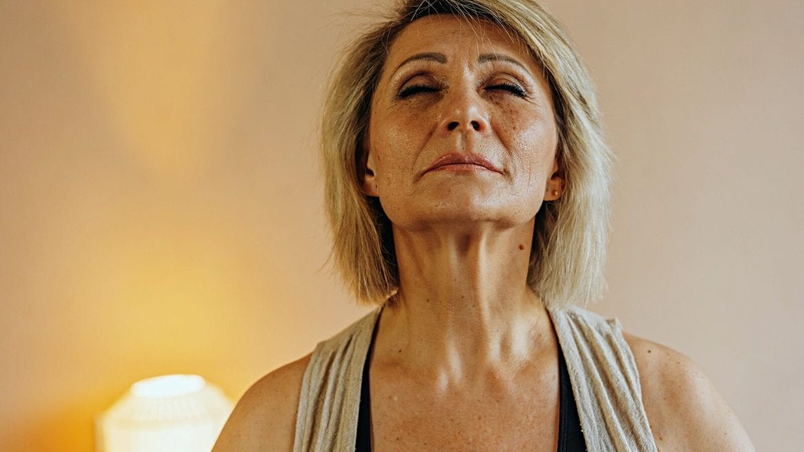 A person with closed eyes, head slightly tilted back, appearing to be in a relaxed state, indoors with soft lighting