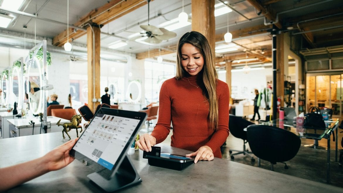 A woman in a red sweater is using a card at a payment terminal on a counter in a bright and spacious shop